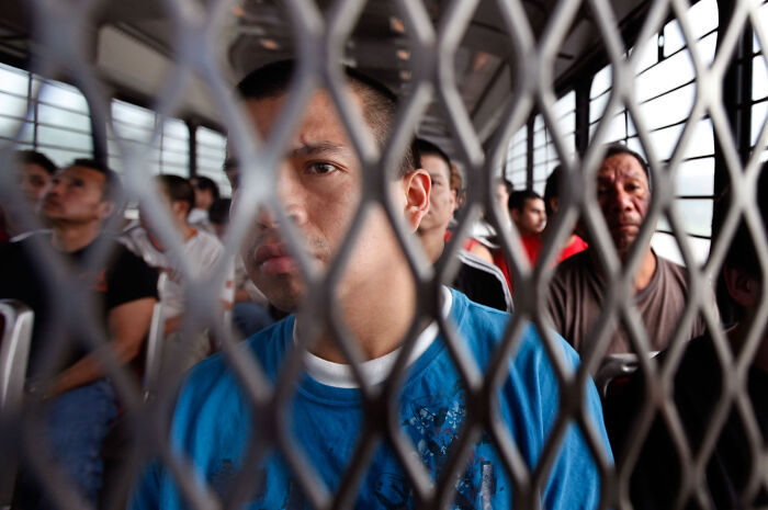 Asylum seekers behind a metal fence, illustrating immigration issues and global bargaining chips in US immigration policy.