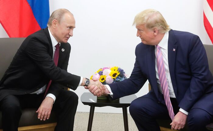 Donald Trump and Vladimir Putin shaking hands during a formal meeting, related to audio threatening Moscow.