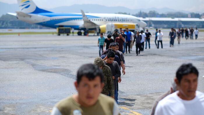 Group of people walking in line on airport tarmac near airplane, illustrating deportation and American citizens topic.