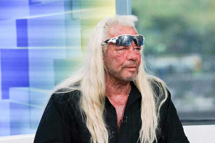 Dog The Bounty Hunter with long blonde hair and sunglasses, appearing in a studio setting during an interview.