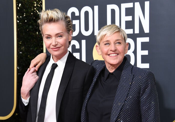 Ellen DeGeneres and Portia de Rossi smiling together at the Golden Globe Awards event, dressed in formal attire.