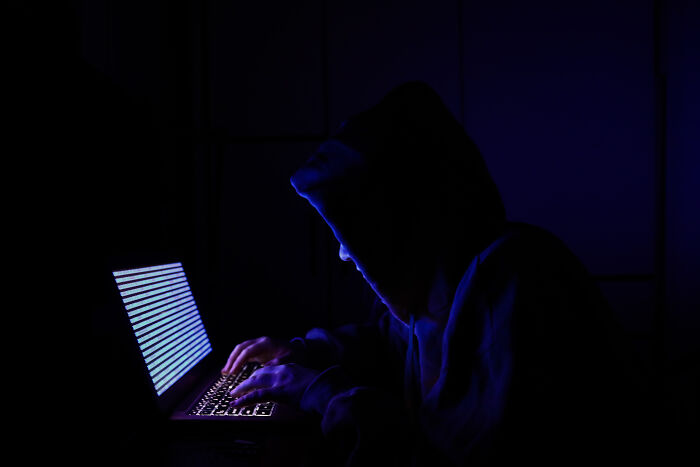 Hacker in dark hoodie typing on laptop, symbolizing threats to expose 100GB of stolen Trump staff emails.