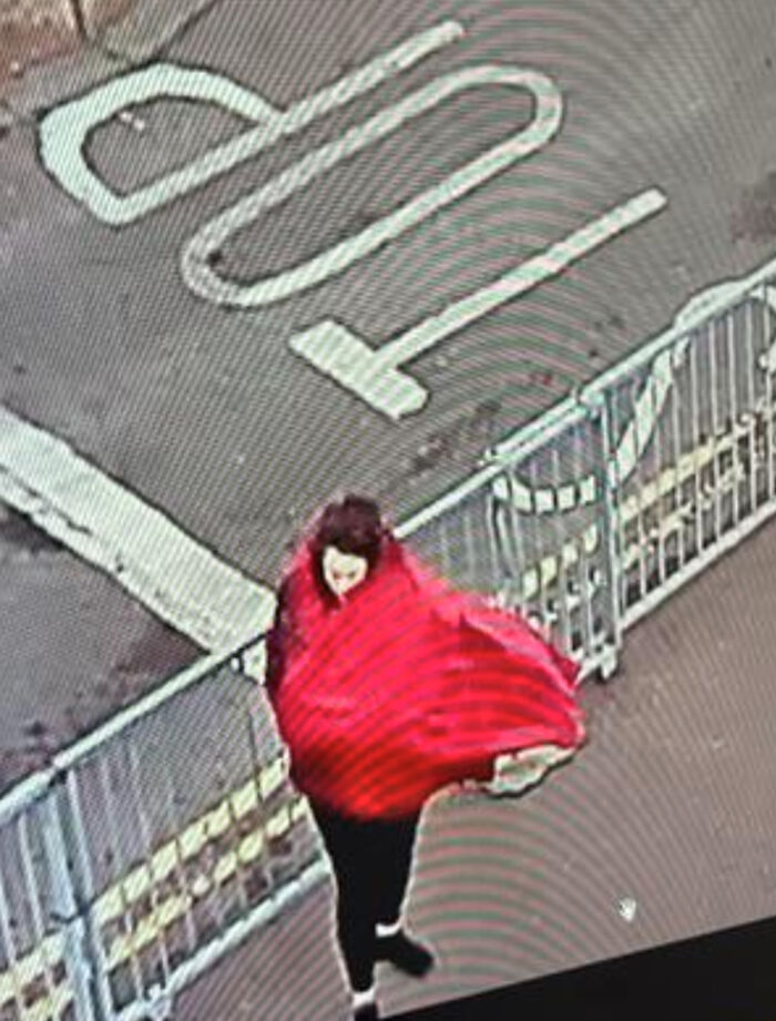 Woman wrapped in a red cloak walking outdoors near metal railings, related to Aristocrat Constance Marten and partner case.
