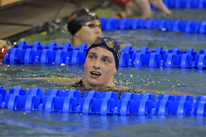 Trans swimmer Lia Thomas wearing swim cap and goggles in pool, competing in swim event with blue lane dividers.