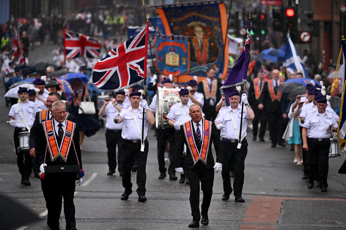 Members of a parade marching with flags and banners during a controversial bonfire event sparking outrage over racism.
