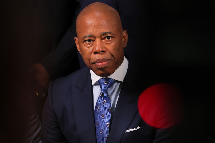 Man in dark suit and patterned blue tie looking serious while attending an event about Zohran Mamdani SAT scores controversy.