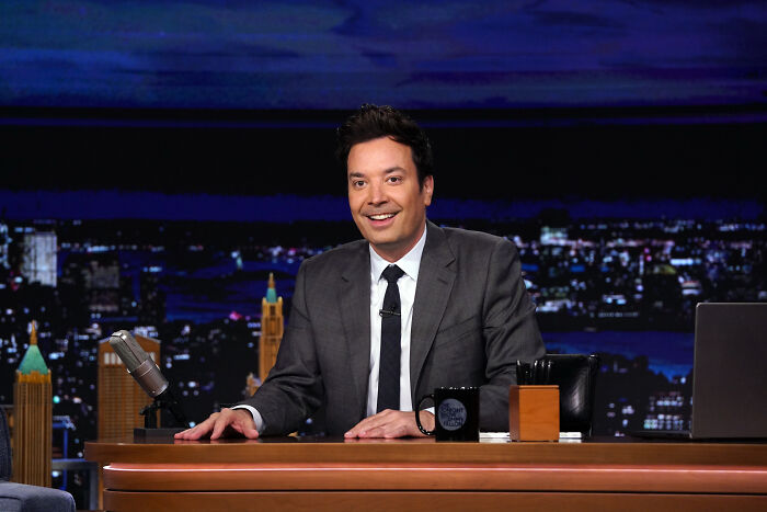 Jimmy Fallon sitting at the late night TV desk, smiling during a broadcast amid Donald Trump TV criticism.