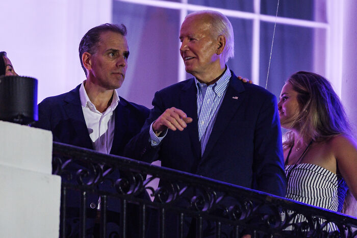 Hunter Biden talking with President Joe Biden on a balcony at an evening event with purple lighting.