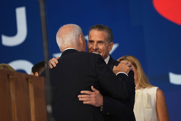 Hunter Biden smiling while embracing President Joe Biden at a public event with a blue backdrop.