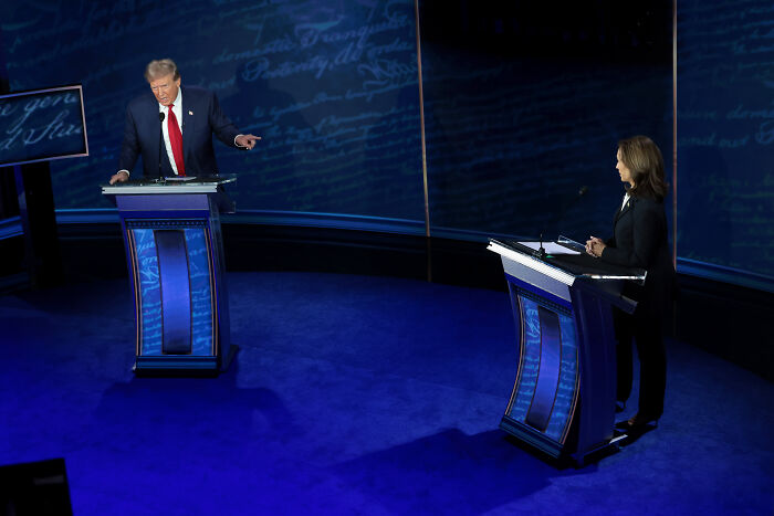 Donald Trump and a woman standing at debate podiums under blue lighting, highlighting Trump accusations in Epstein context.