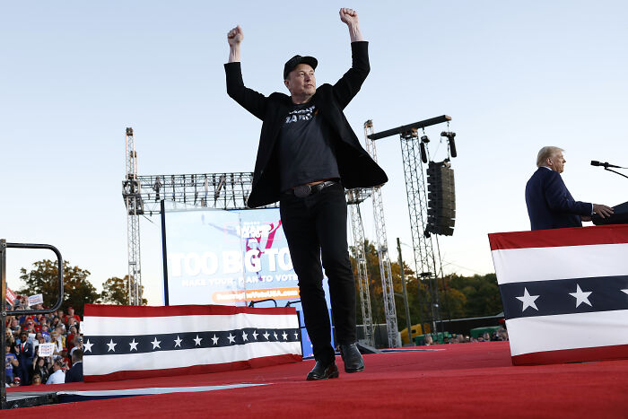 Elon Musk on stage at a rally with arms raised, hinting at launching a new political party in the US.