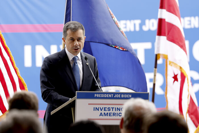 Pete Buttigieg speaking at podium with American flags, leading 2028 Democratic primary poll as openly gay candidate