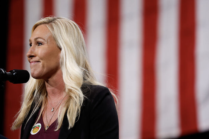 Marjorie Taylor Greene speaking at event with American flag background, addressing Gaza situation and genocide keyword topic.
