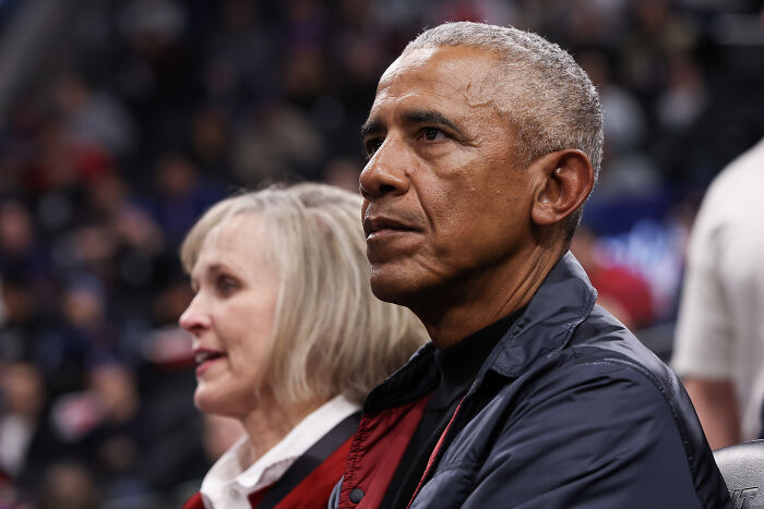 Barack Obama seated and looking ahead, focused during an event discussing allegations and political controversy.