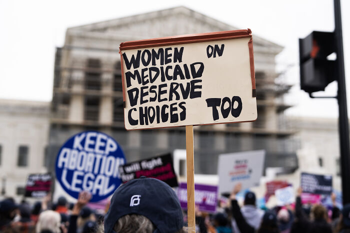 Protesters outside government building hold signs about Medicaid and rights amid concerns over medical data access by ICE.