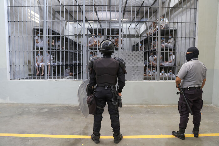 Two riot police officers stand in front of a jail cell with inmates, reflecting tensions around American citizens deported.