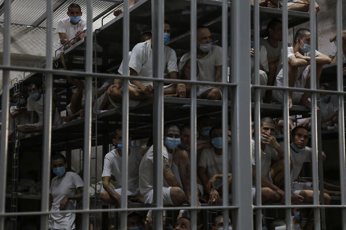 Prisoners in El Salvador jail wearing masks, overcrowded conditions highlighting threats from gangs and harsh treatment concerns.