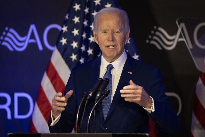 President Joe Biden speaking at a podium with American flags, illustrating 2024 presidential election impact on young Americans' mental health.
