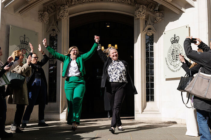 Two women celebrating outside a government building with onlookers, related to U.K. PM Starmer and trans people single-sex spaces debate.