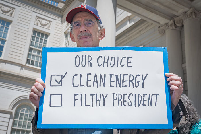 Man holding a protest sign advocating clean energy outside a government building, referencing climate change action debate.