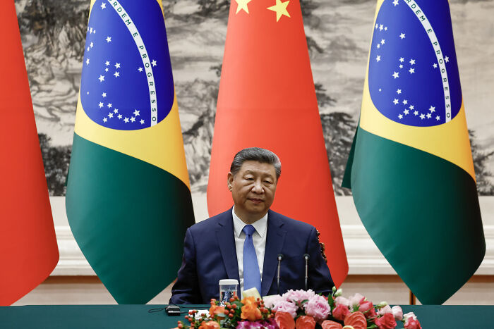 Chinese leader sitting at a conference table with Brazil and China flags, related to audio of Donald Trump threatening Moscow.