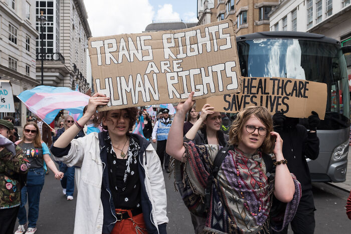 Protesters hold signs supporting trans rights and healthcare in a city street during a demonstration on trans people in single-sex spaces.