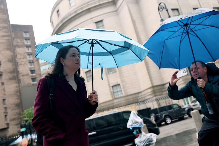 Woman holding blue umbrella outside courthouse during high-profile DOJ prosecution related to James Comey&rsquo;s daughter.