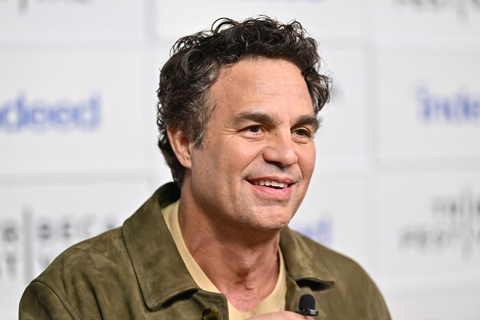 Mark Ruffalo speaking at an event, wearing a green jacket, addressing issues related to Joe Rogan and ICE raids.