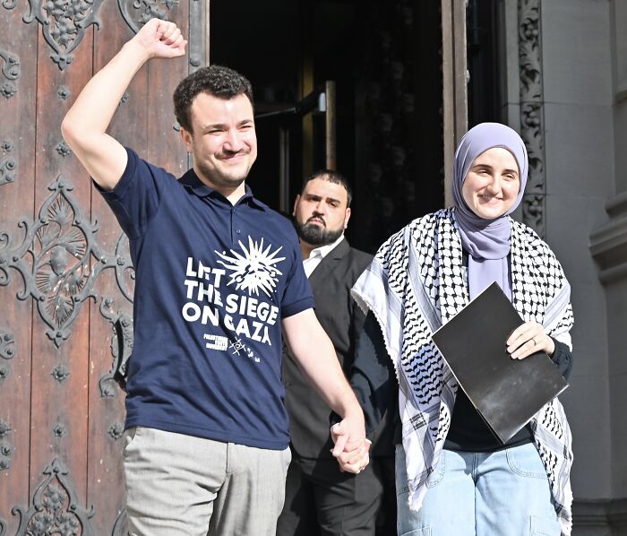 Mahmoud Khalil raising fist, wearing Let The Siege On Gaza shirt, standing with woman in hijab after ICE detention and Trump claim.
