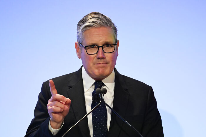 U.K. PM Starmer speaking at a podium, wearing glasses and a dark suit, addressing trans people and single-sex spaces policy.