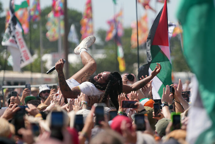 Bob Vylan crowd surfing at a concert amid colorful flags, capturing the rap duo blocked entry by State Department.