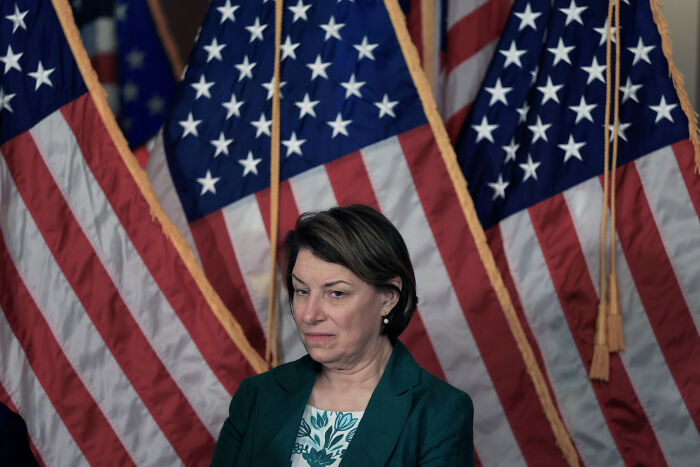 Senator Murkowski standing before multiple American flags, reacting to swing-vote decision on GOP bill amid criticism.