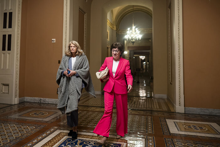 Two women walking in a hallway with intricate tile flooring discussing the swing-vote Murkowski on GOP bill decision.