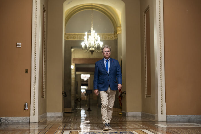 Man walking in a hallway under chandelier representing swing-vote Murkowski casting decisive yes on GOP bill.