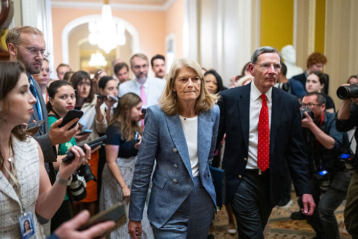 Senator Murkowski walking through a crowded hallway amid media coverage after casting a decisive swing-vote on GOP bill.