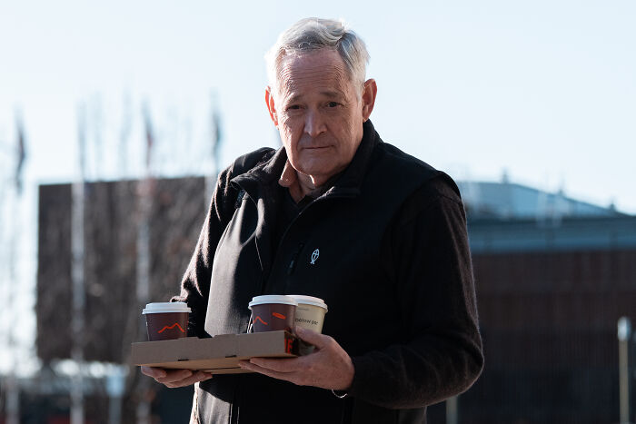 Older man holding takeaway coffee cups outdoors, related to mushroom poisoning case and jury verdict updates.