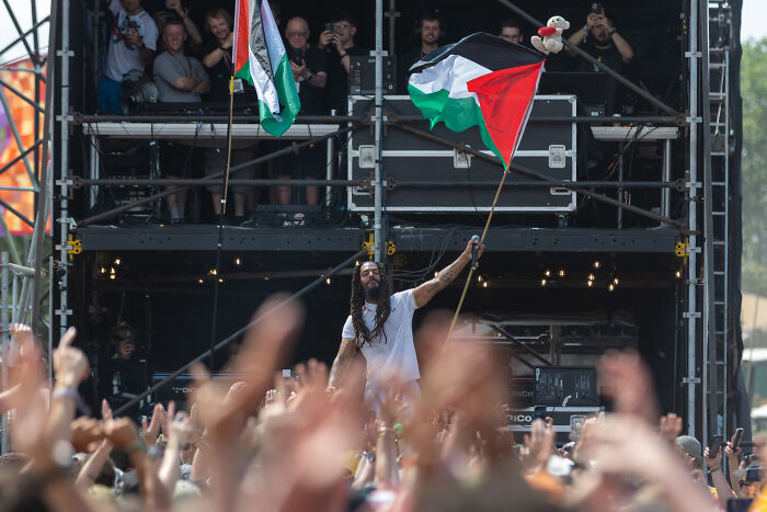 Performer waving Palestinian flag onstage amid crowd at Royal Opera House during tense and chaotic moment.