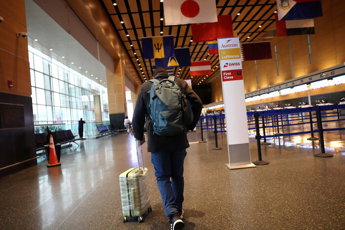 Person with backpack and suitcase walking through airport terminal, illustrating immigrant families facing fear of separation.