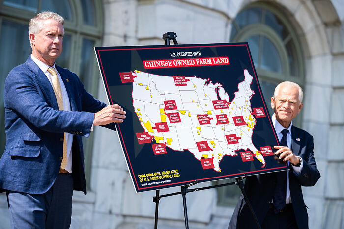 Two men hold a map showing counties with Chinese owned farm land amid agriculture and farmworker policy discussion.