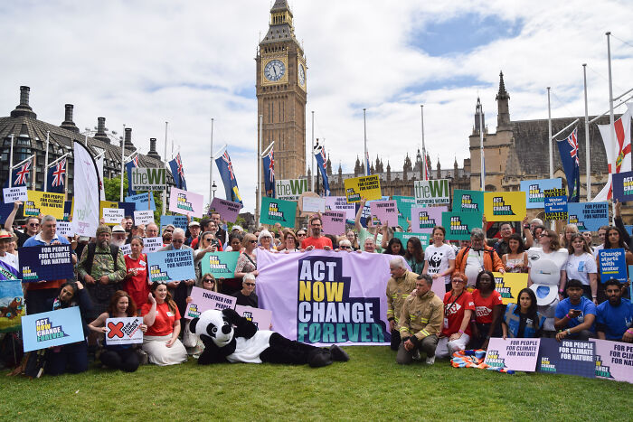 Climate change protest with diverse group holding signs near Big Ben, highlighting activism and legal actions between countries.