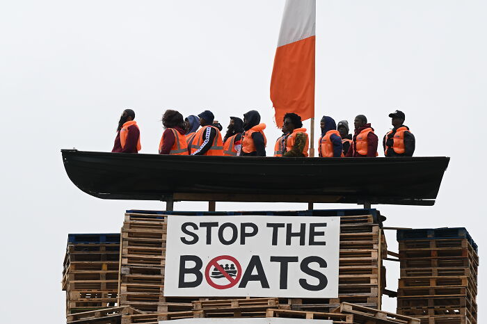 Mock migrant boat on bonfire structure with Stop the Boats sign, sparking outrage over racist display.