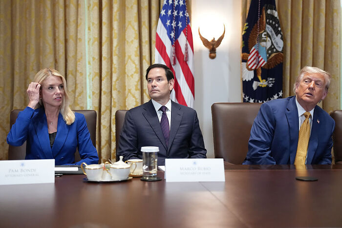 Donald Trump with Pam Bondi and Marco Rubio seated at a table during a discussion, U.S. flags in the background.