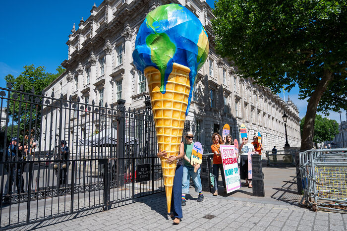 Protesters outside a government building hold signs and a large melting earth ice cream cone about climate change legal actions.