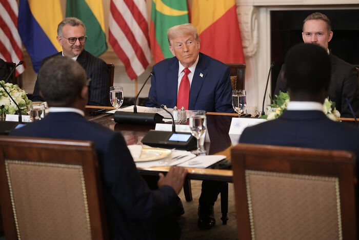 Donald Trump in a formal meeting discussing immigration policies and asylum seekers at a table with international delegates.