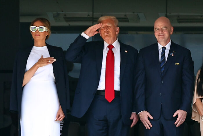Donald Trump saluting during Club World Cup trophy presentation as crowd boos in the background.