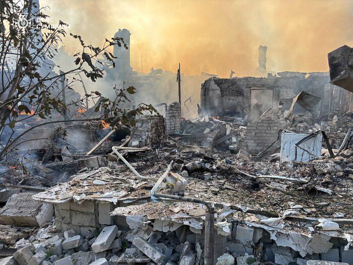 Ruined buildings and smoke rising in a war-torn area, highlighting conflict related to Ukraine arms and Putin.