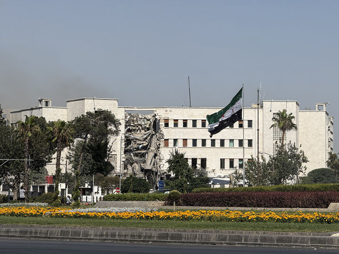 Damaged government building in Syria with a flag flying, symbolizing ongoing fighting and Israel's involvement in the conflict.