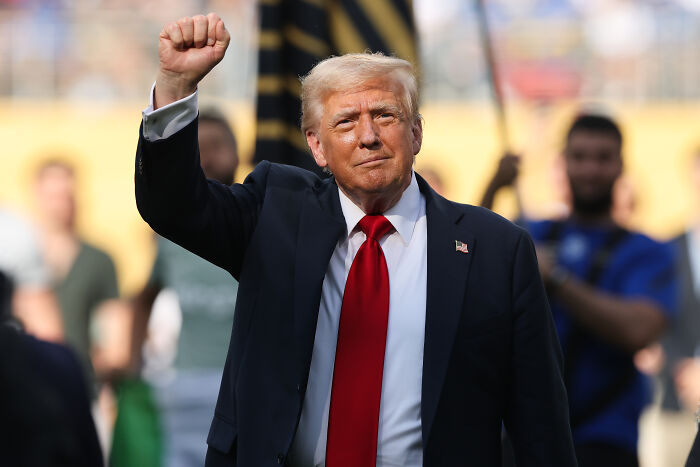 Donald Trump raising fist during Club World Cup trophy presentation with crowd booing in the background.