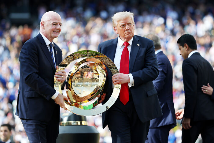 Former President Trump holding the gold Club World Cup trophy while FIFA officials stand nearby at a stadium event.