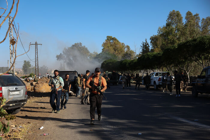 Armed men walking along a road amid ongoing fighting in Syria, illustrating conflict and Israel involvement.